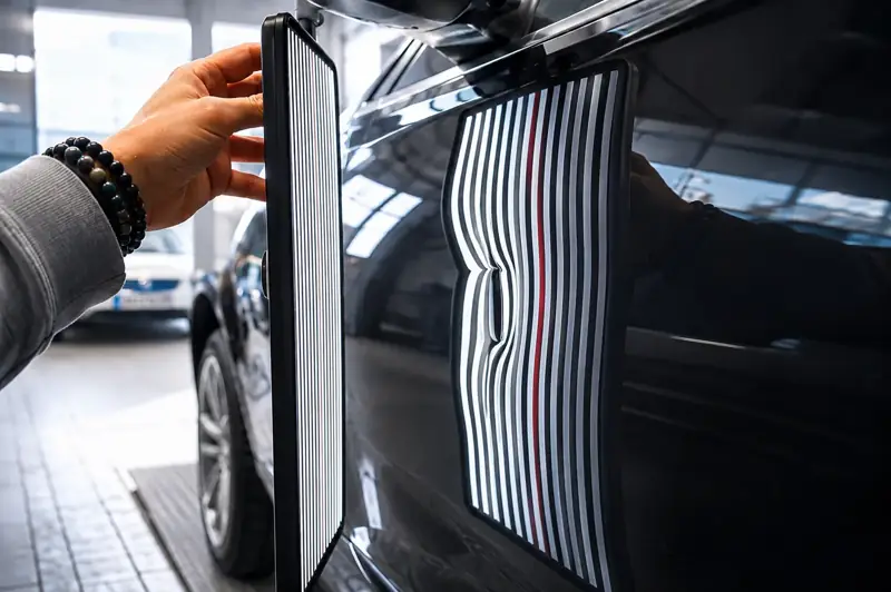 Streifenlicht-Tafel an der Seitenwand eines schwarzen Autos, die verzerrten Linien zeigen eine Delle