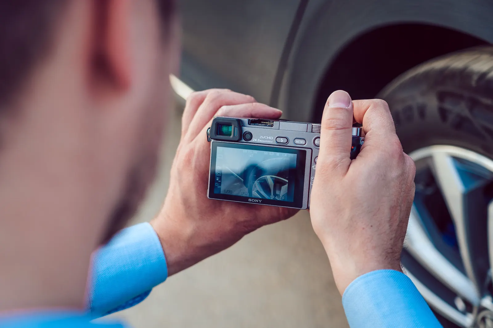 Michael Dorzweiler fotografiert mit einer Systemkamera das Rad eines Autos, Blick über die Schulter
