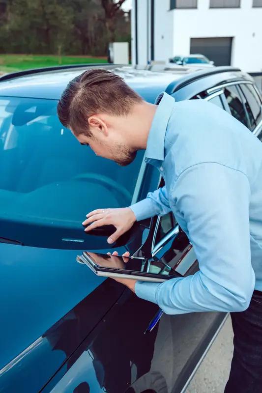 Michael Dorzweiler prüft mit dem Tablet in der Hand die Windschutzscheibe eines dunkelblauen Autos