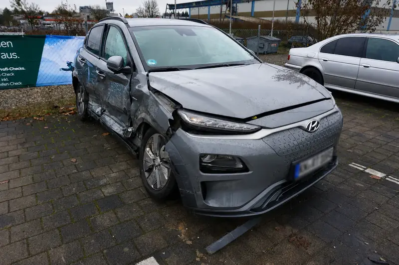 Grauer Hyundai Kona Elektro mit Unfallschaden an Front und Fahrerseite auf einem Parkplatz
