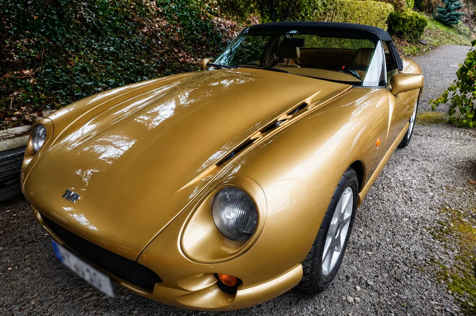 Goldfarbener TVR-Roadster mit geschlossenem Stoffverdeck auf einer Einfahrt