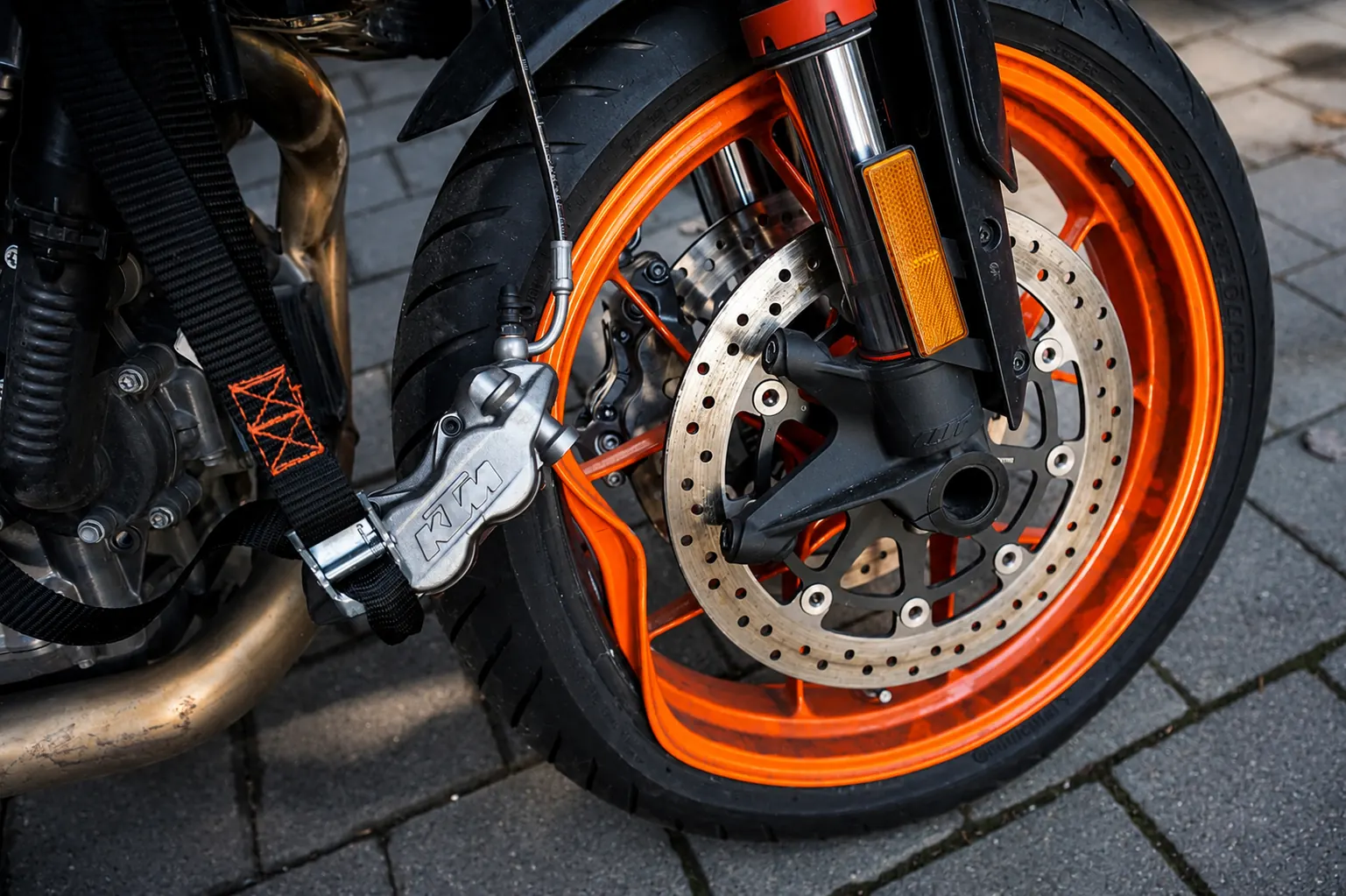Vorderrad einer KTM mit orangefarbener Felge, Bremsscheibe und Bremssattel, gesichert mit Spanngurt
