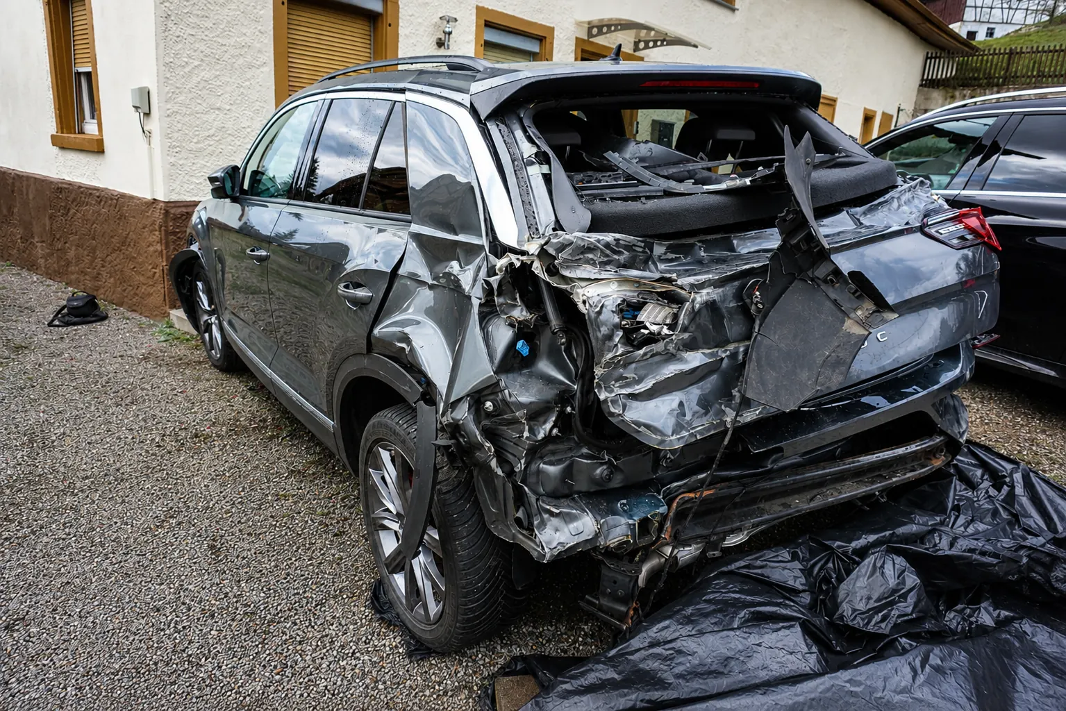 Graues SUV mit völlig zerstörtem Heck, abgestellt auf einem Kiesplatz