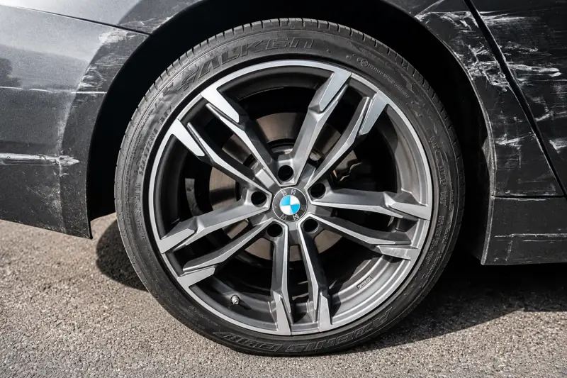 Kratzer und Schrammen an Radlauf und Seitenteil eines dunkelgrauen BMW neben der Alufelge