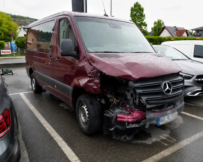 Dunkelroter Mercedes Sprinter mit eingedrückter Front auf einem Parkplatz