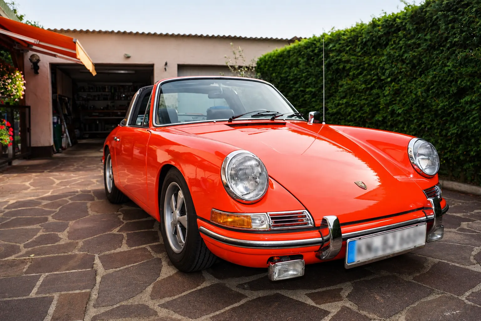 Orangefarbener Porsche 911 der ersten Generation mit Chromstoßstangen vor einer Garage